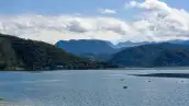 Un cuerpo de agua rodeada de tres montañas de color verde bajo un cielo con nubes blancas.jpg