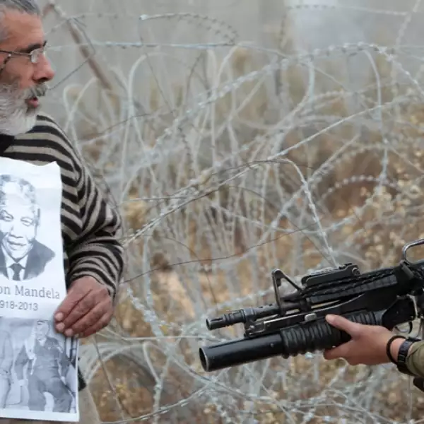 un palestino muestra una fotografia de nelson mandela a soldados israelies