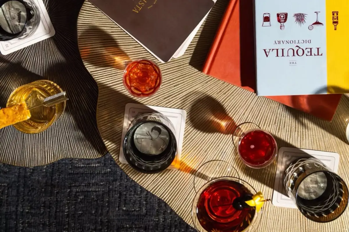 Foto de una mesa vista desde arriba del bar Jewel of the South en Nueva Orleans con siete vasos servidos con distintos cocteles y dos libros sobre mixología