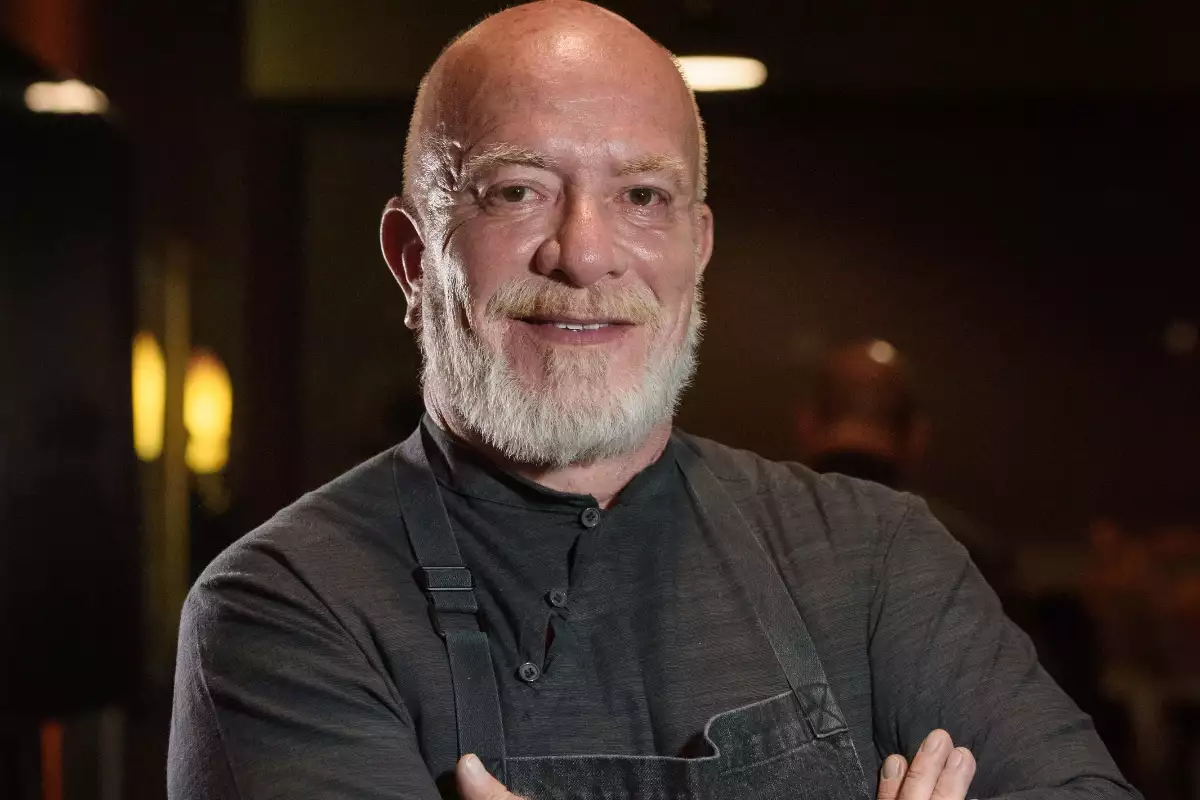Foto del chef Gerardo Vázquez Lugo, vestido con camisa de lino oscuro, delantal negro y una tupida barba blanca.
