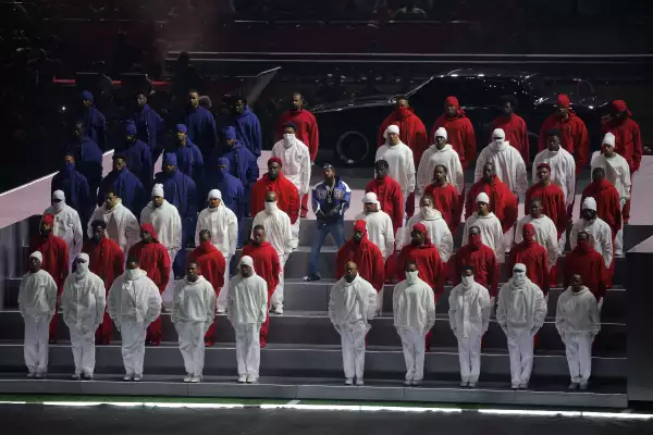 Foto de Kendrick Lamar al centro, a ambos lados de él están formados bailarines vestidos de rojo, azul y blanco formando la bandera de Estados Unidos dividida por la mitad.