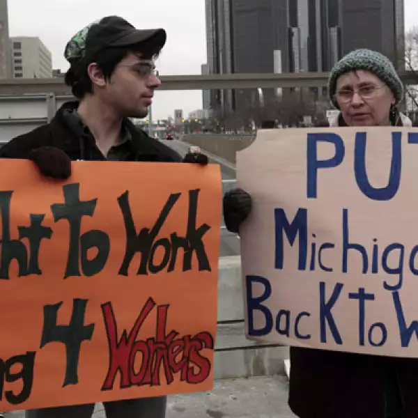 Dos manifestantes con mantas en una protesta por los derechos de los trabajadores, frente a la sede del evento.
