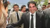Jorge Kahwagi vestido de traje negro y con una sonrisa. Detrás de él otros hombres con traje.jpg