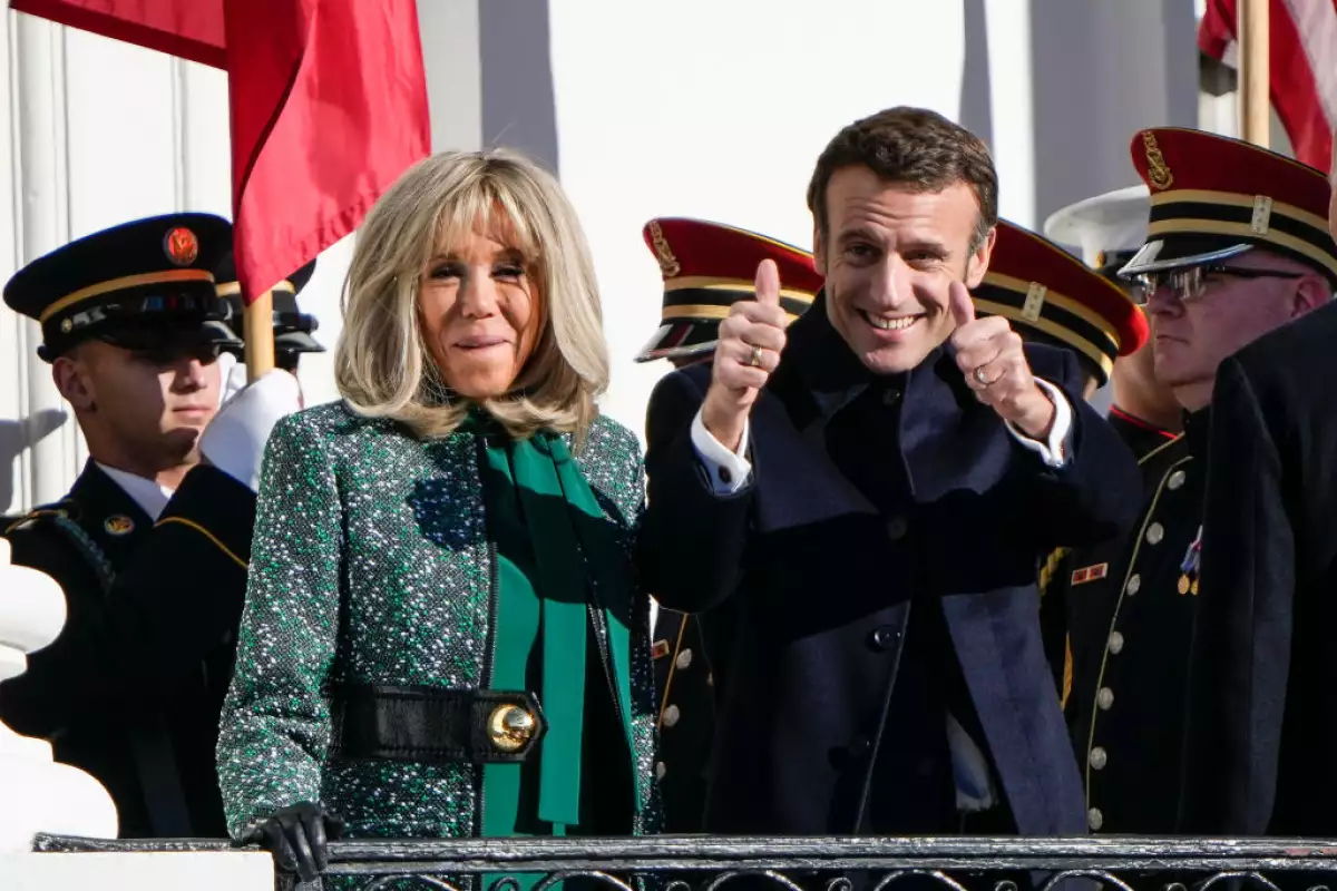 Foto de Emmanuel Macron levantando los dedos pulgares y sonriendo y su esposa Brigitte Macron a su lado.