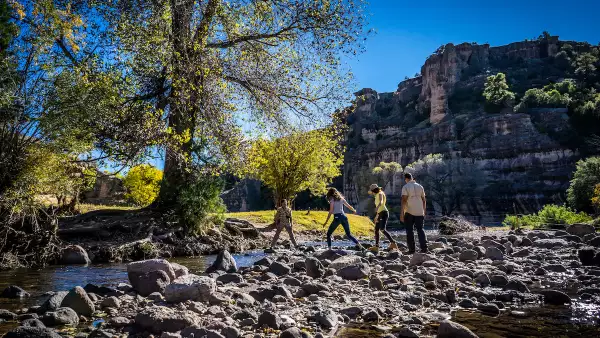 Imagen de cuatro jóvenes cruzando un arroyo y con la sierra de fundo.