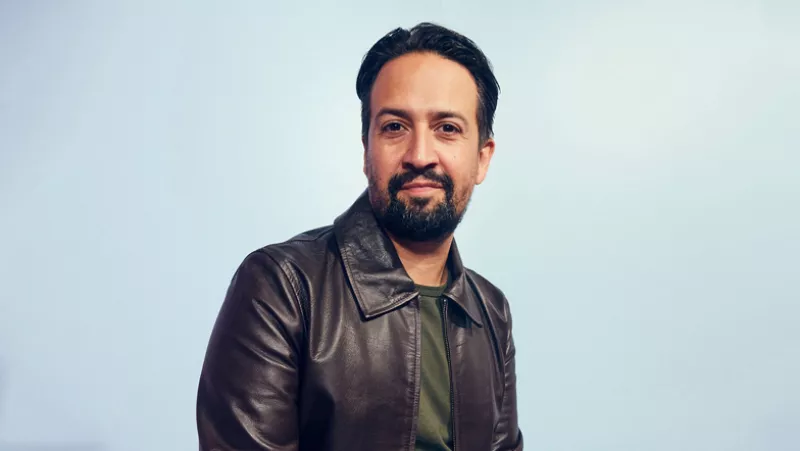 Foto de Lin-Manuel Miranda con chaqueta de piel café oscuro y sonriendo levemente a la cámara.