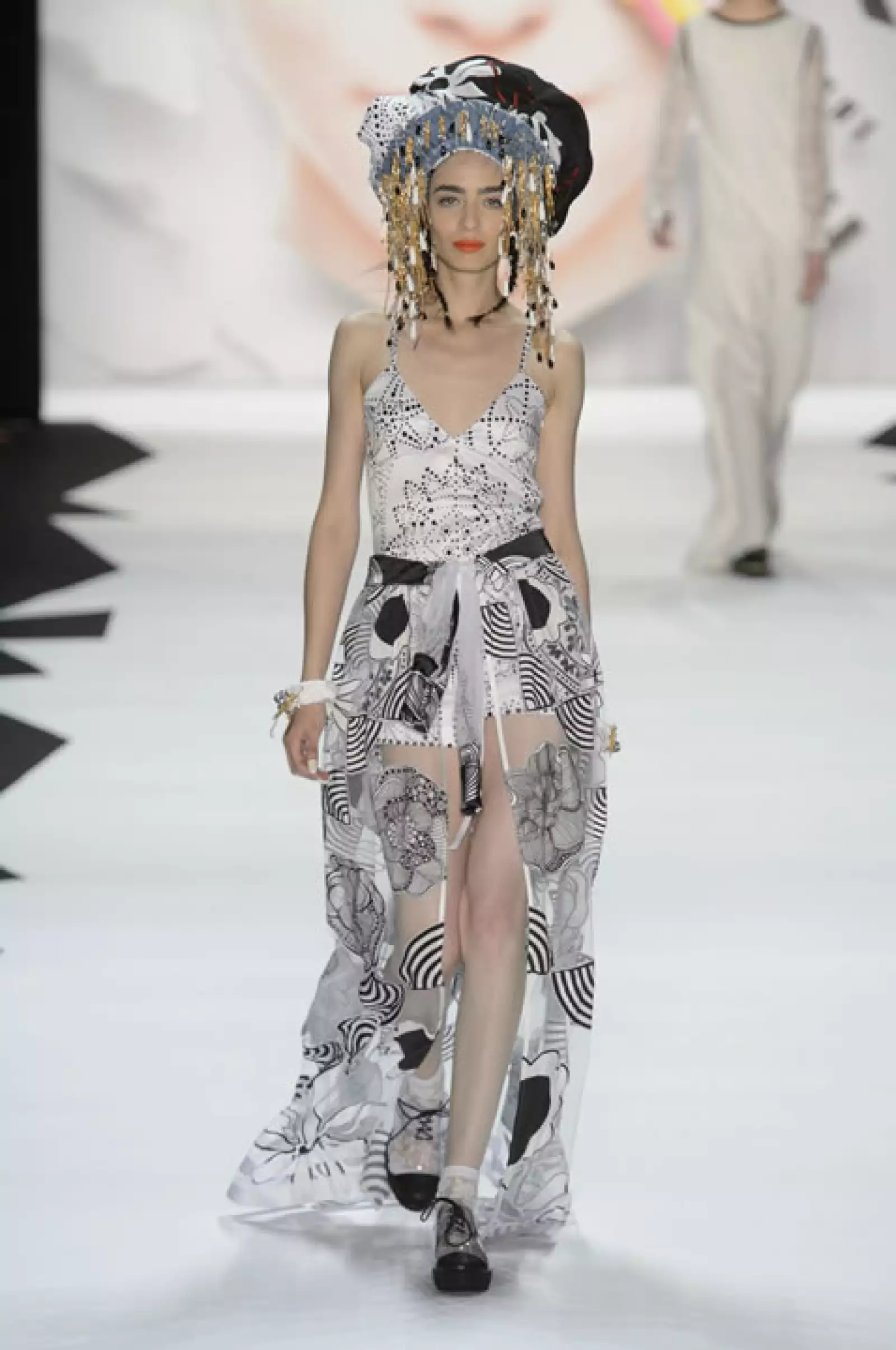 Jumpsuit blanco de satín con aplicaciones de jacquard, túnica de patchwork usada como falda y sandalias de plataforma.