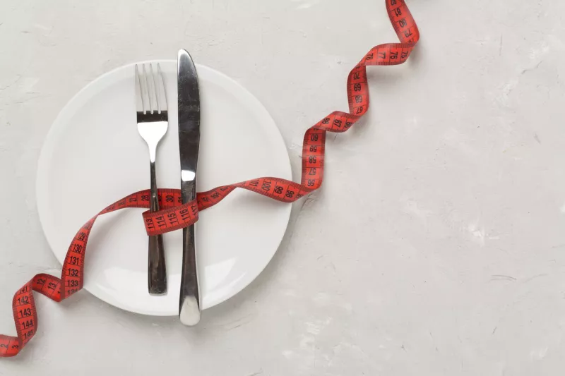 Measuring tape with empty plate on concrete background, top, view. Weight loss concept