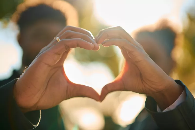 Couple forming heart shape with hands against sunlight
