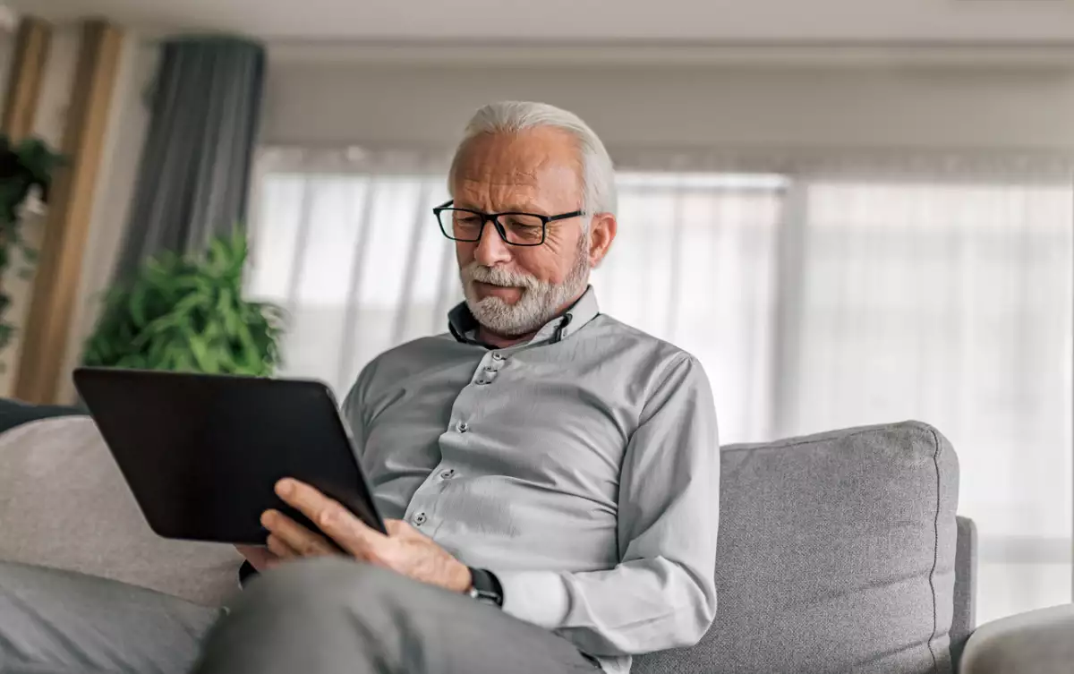 Smiling elderly businessman using digital tablet while sitting on couch at home