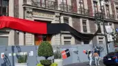 Sucursal cerrada de Nacional Monte de Piedad, con banderas y símbolos rojos y negros, gente camino a las afueras.