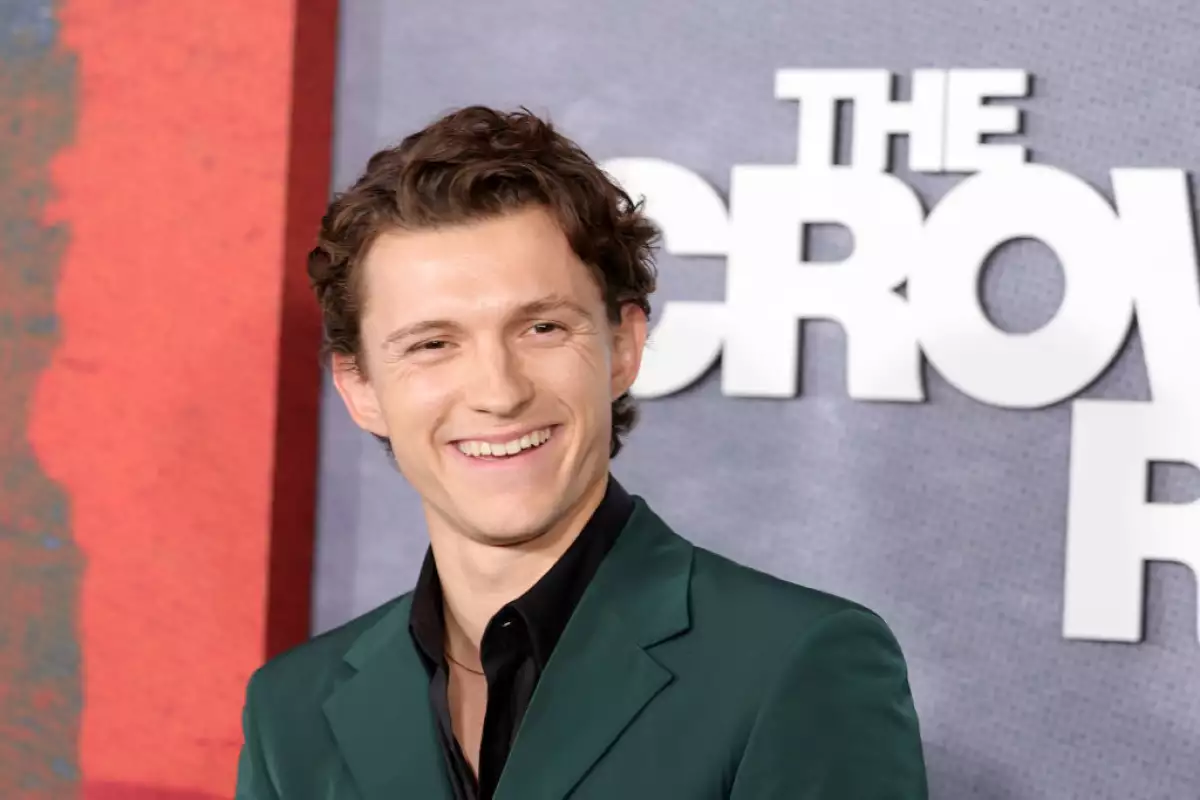 Foto de Tom Holland sonriendo con saco color verde, camisa negra y el letrero de The Crowded Room detrás.