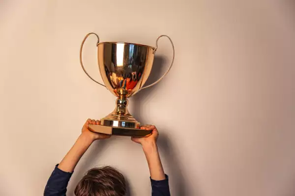 Champion cup in hands of kid on beige background