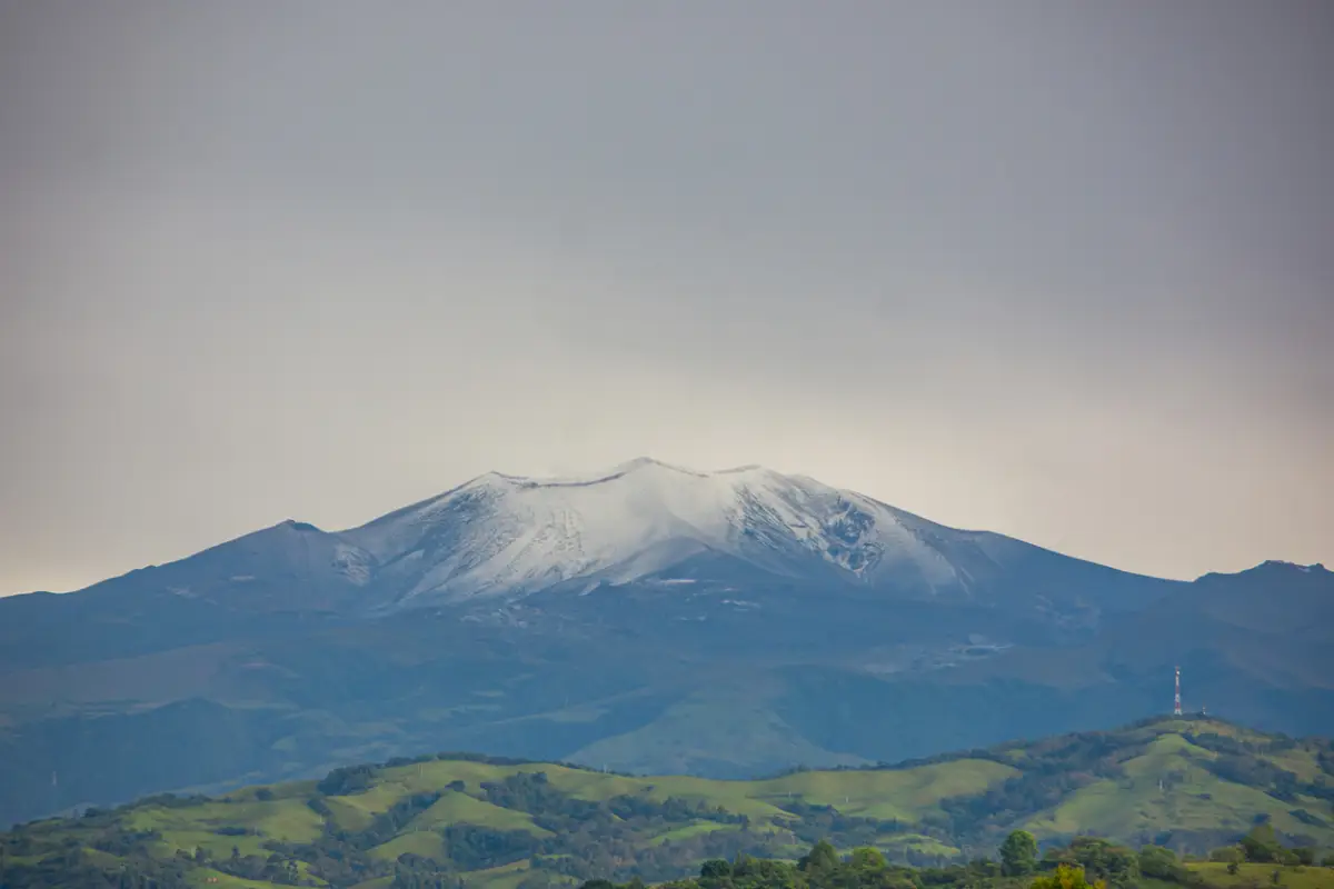Una vista impresionante del volcán Puracé cubierto de nieve, rodeado de colinas verdes en Popayán, Cauca, Colombia. La majestuosa belleza de la naturaleza.