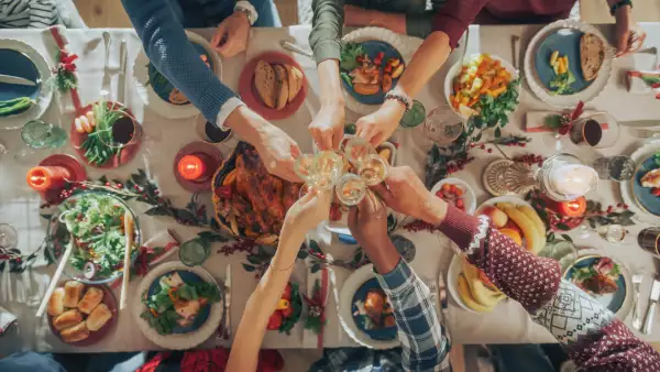 Foto de una mesa vista desde arriba llena de platillos navideños y una familia brindando con las copas al centro