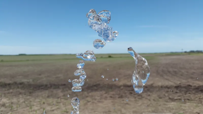 Chorro de agua en primer plano, de fondo un campo a medio sembrar.
