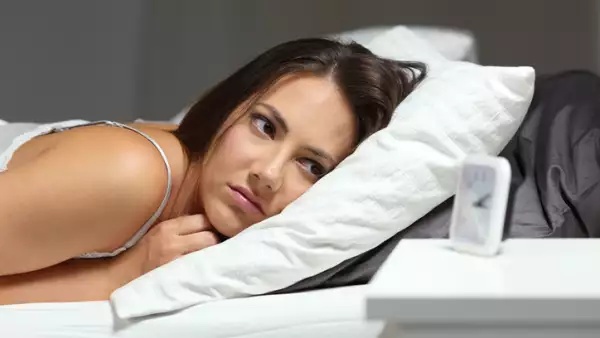 Sleepless insomniac girl looking at alarm clock in the night