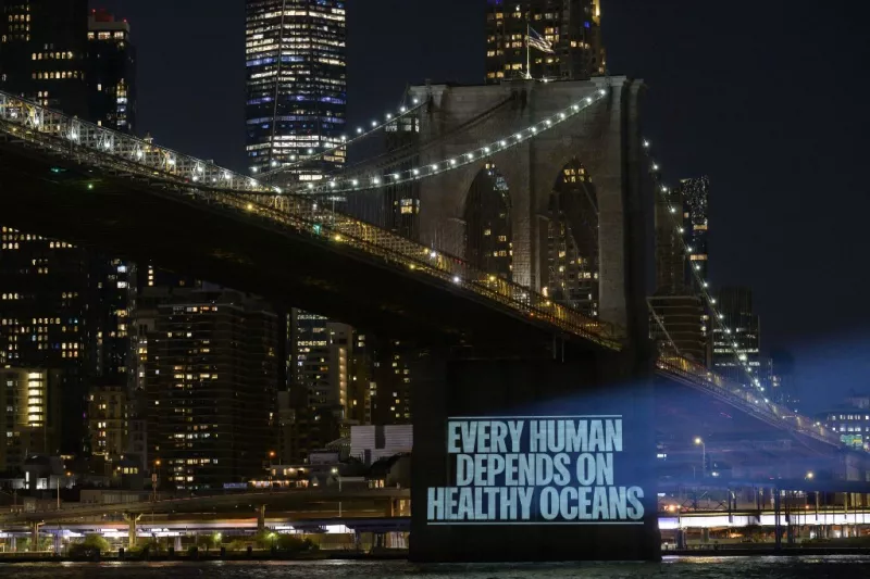 En esta foto de archivo tomada la noche del 14 de agosto de 2022, Greenpeace proyecta imágenes que llaman a la acción para finalizar un Tratado Global de los Océanos en el puente de Brooklyn en la ciudad de Nueva York. En la foto aparece el mensaje, en inglés, "Todo humano depende de los océanos sanos". 
