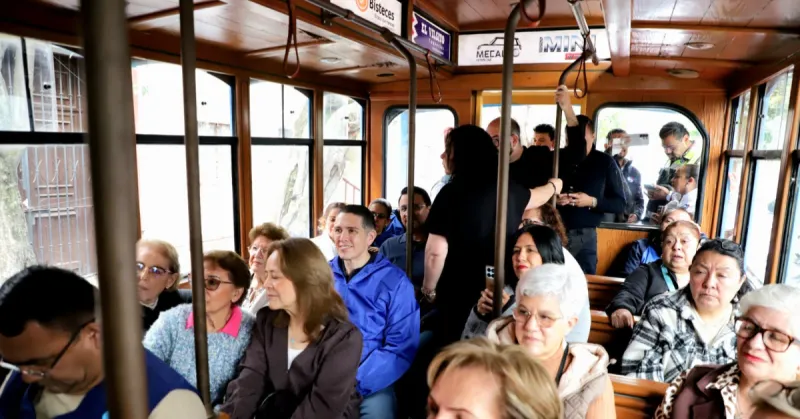 Interior de un tranvía en donde viajan 14 personas sentadas y cuatro paradas. El color del tranvía es café.jpg