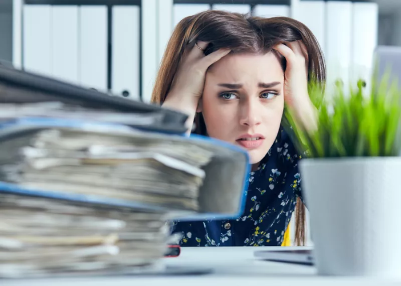 Tired and exhausted woman looks at the mountain of documents propping up her head with her hands