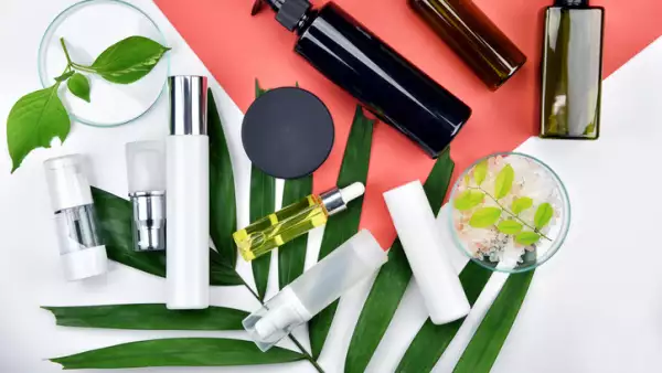 Cosmetic bottle containers with green herbal leaves, Blank label for branding mock-up, Natural beauty product concept, Flat lay on color background.