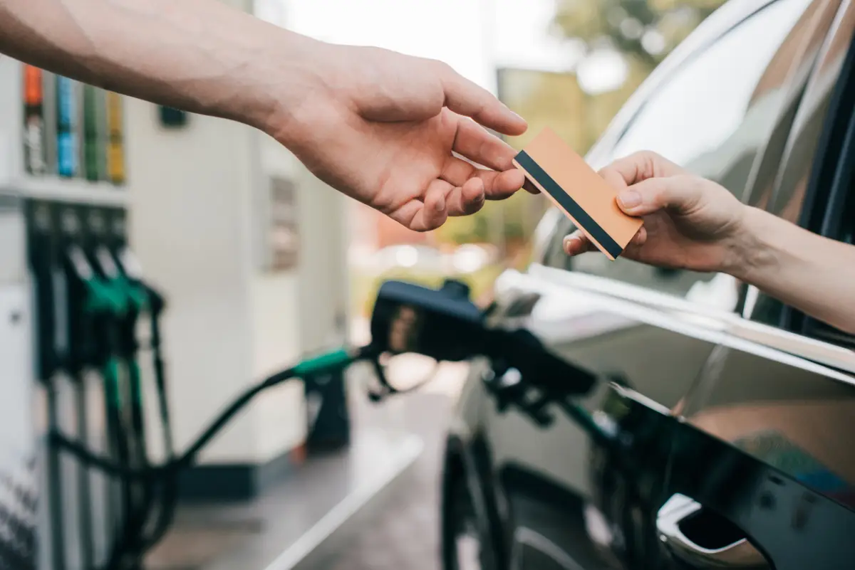 Un usuarios cargando combustible en una estación de servicio mientras el despachador cobra al usuario con tarjeta.