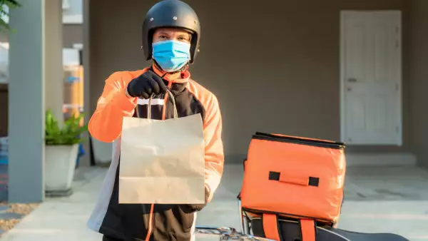 Delivery Asian man wear protective mask in orange uniform and ready to send delivering Food bag in front of customer house with case box on scooter, express food delivery and shopping online concept.