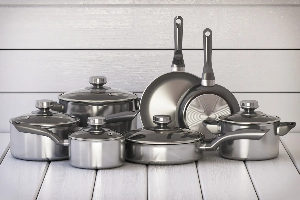Set of stainless pots and pan with glass lids on the white wooden background