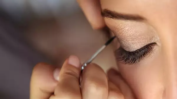 Beautiful fashion model applying makeup by makeup artist.