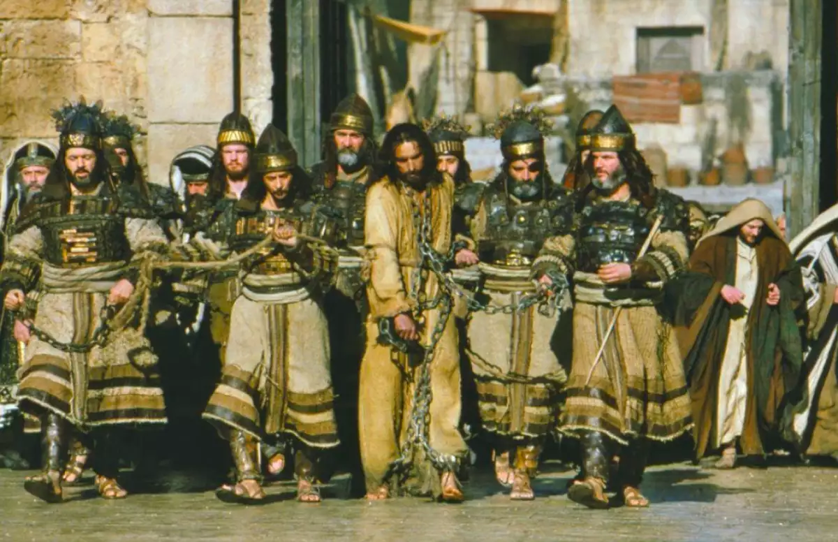 fotograma de la pelicula La pasión de Cristo, en el que se muestra a Jesús encadenado y rodeado de soldados romanos.