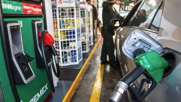Un trabajador atiende el suministro de gasolina Magna a un automóvil, mientras limpia su parabrisas. 