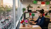 Mujer sentada frente a un escritorio en una oficina adornada con decoraciones patrias por la Independencia de México, su lugar está frente a una ventana que da hacia la calle, donde se ve un desfile. 