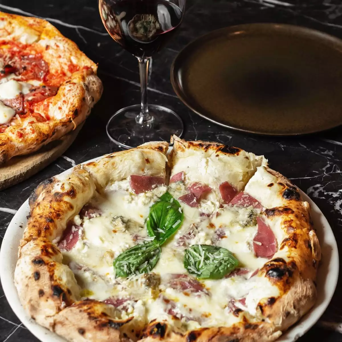 Pizzas sobre mesa del restaurante Fratelli La Bufala con una copa de vino para acompañar