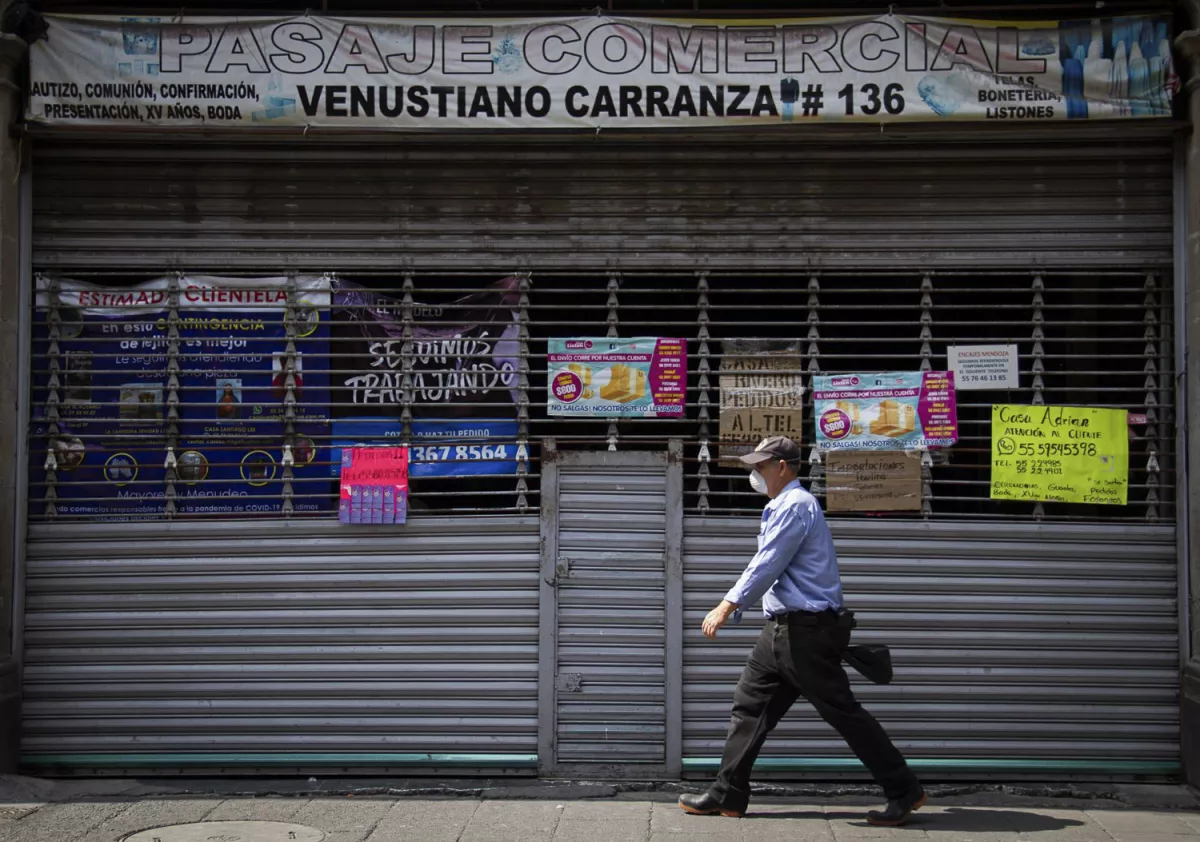 Un hombre camina por la Calle Venustiano Carranaza en el Centro Histórico, frente a el, una plaza cerrada con diversos letreros con invitaciones de los comerciantes a contactarlos vía telefónica