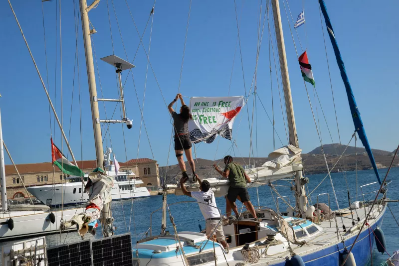 La gente cuelga una pancarta antes de la salida de los veleros Electra y Oxygen, parte de la Flotilla Global de Sumud, desde el puerto de Ermoupolis en la isla de Siros, Grecia, el 14 de septiembre de 2025.