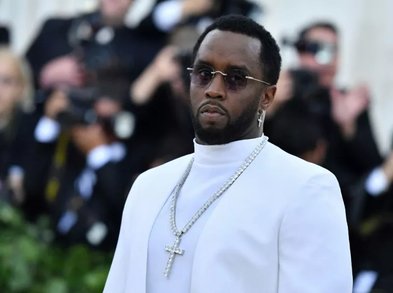 Foto de Sean Diddy Combs en la Met Gala de 2018, vestido con traje blanco, una cadena con cruz de diamantes y lentes oscuros.