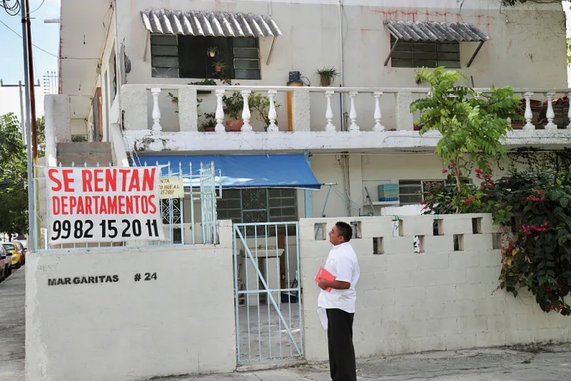 Un hombre parado frente a una casa con un letrero que dice "se rentan departamentos". 