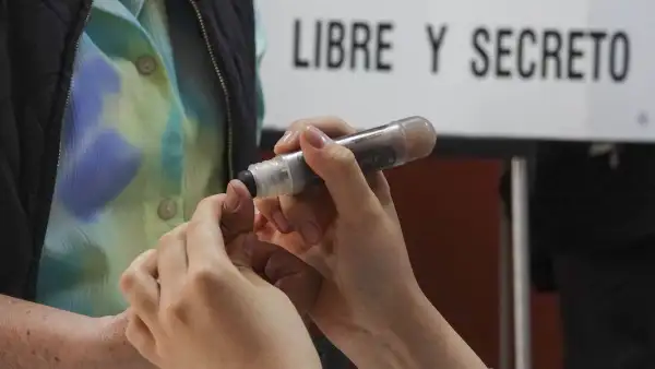 Funcionario de casilla aplica tinta electoral en el pulgar de un votante