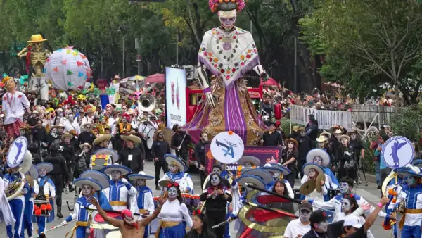 Dos catrinas gigantes con huipiles. Hombres y mujeres vestidos de blanco y azul con maquillaje de catrinas.jpg