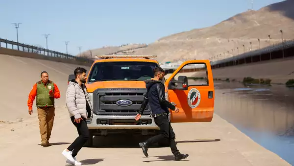 Asylum-seeking migrants run before crossing the Rio Bravo river to turn themselves in to U.S Border Patrol agents to request asylum in El Paso, Texas, U.S., as an agent of the Mexican immigrant welfare agency Grupo Beta watches them in Ciudad Juarez