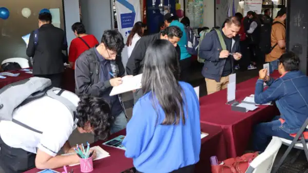 Un total de nueve jóvenes en una mesa roja llenando ofertas de empleo, una persona está sentada y con un papel en mano.jpg