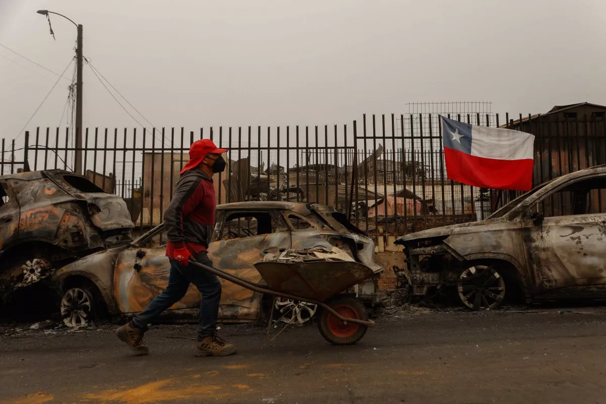 Un residente empuja una carretilla a lo largo de una calle bordeada con los restos carbonizados de vehículos destruidos después de que un incendio forestal devastara Lirquen, una ciudad en Penco cerca de la ciudad de Concepción, Chile, el 20 de enero de 2026. Los bomberos que luchan contra los principales incendios forestales en el sur de Chile que han matado a 20 personas en los últimos cuatro días se beneficiaron del clima más frío a principios del 20 de enero, dijeron las autoridades.