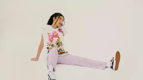 Una mujer con pants rosa, playera blanca con diseño y sneakers vans Knu Skool de Vans.