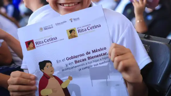 Dos manos de un niño sostienen un sobre blanco con la imagen de Rita Cetina y con el texto: En el Gobierno de México.jpg