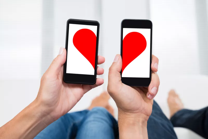 Two People With Mobile Phones Showing Halves Of Heart Shape