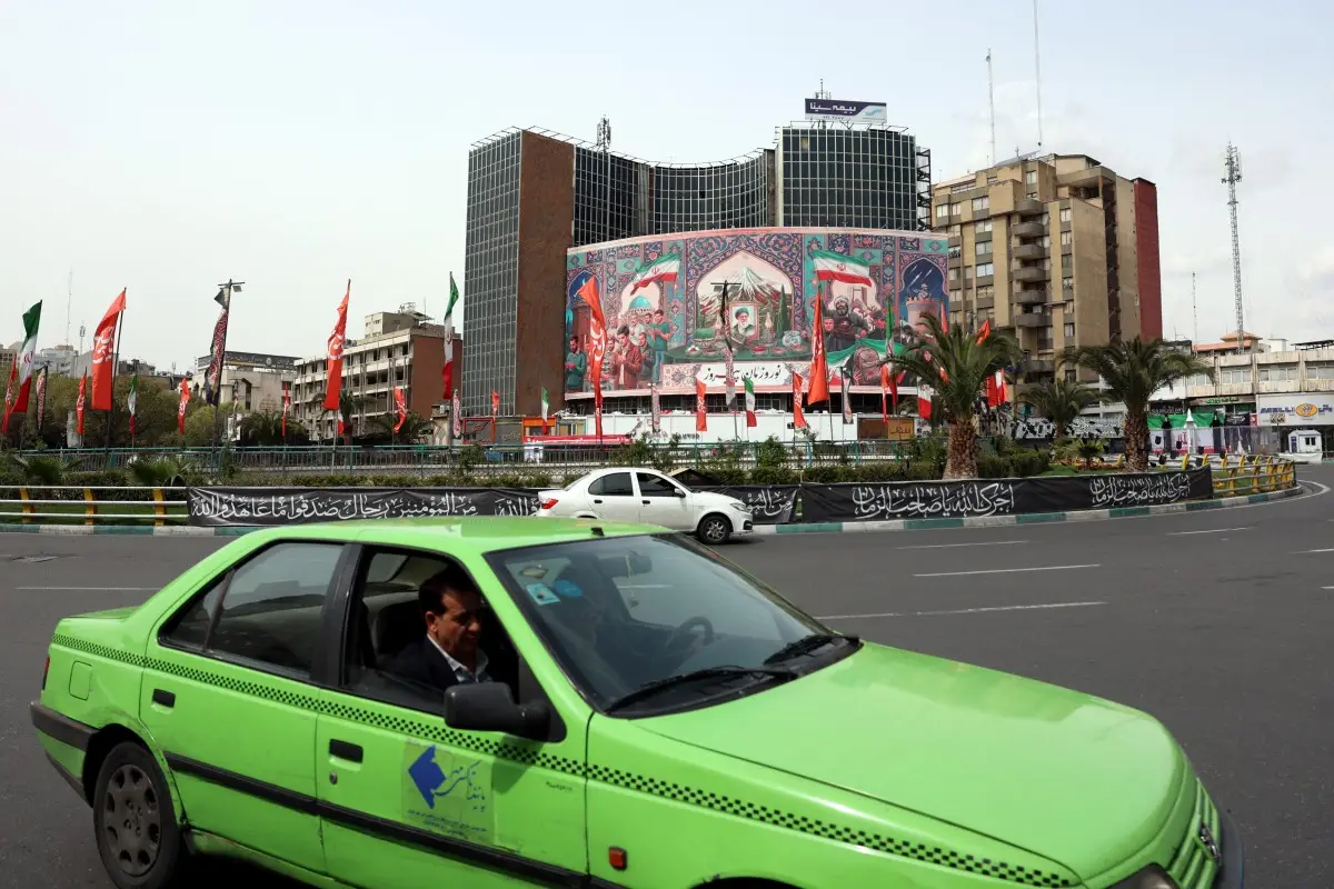 Coches pasan por una valla publicitaria gigante con un retrato del líder supremo asesinado de Irán, el ayatolá Ali Khamenei (C), en la plaza Valiasr de Teherán el 22 de marzo de 2026.