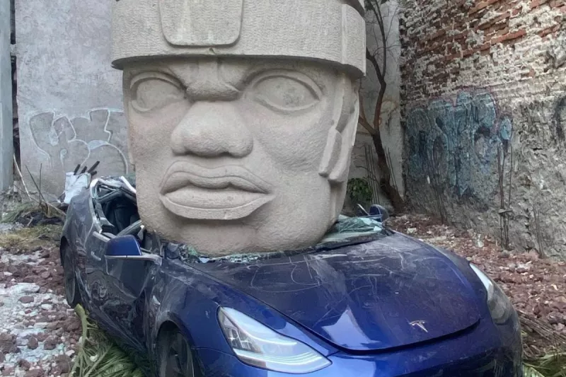 Foto de la escultura de cabeza olmeca sobre un tesla model 3