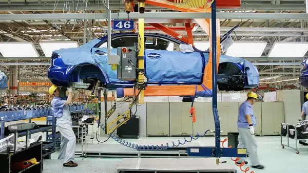 Una línea de ensamble de autos chinos en donde se ve como dos trabajadores ensamblar componentes.