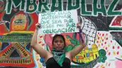 Una mujer joven muestra un cartel con la leyenda "quien elija maternar, que sea por deseo, no por obligación".