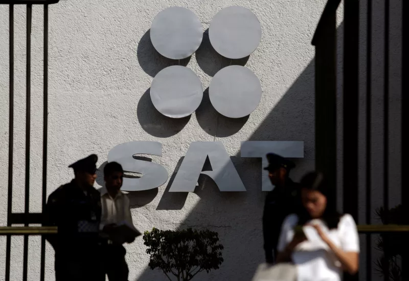 Policemen and people stand in front of the logo of Mexico's Tax Administration Service at the entrance to their premises in Mexico City